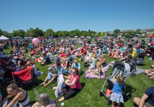 Crowds site on the grass enjoying a performance and the sunshine during the Oakville Children's Festival.