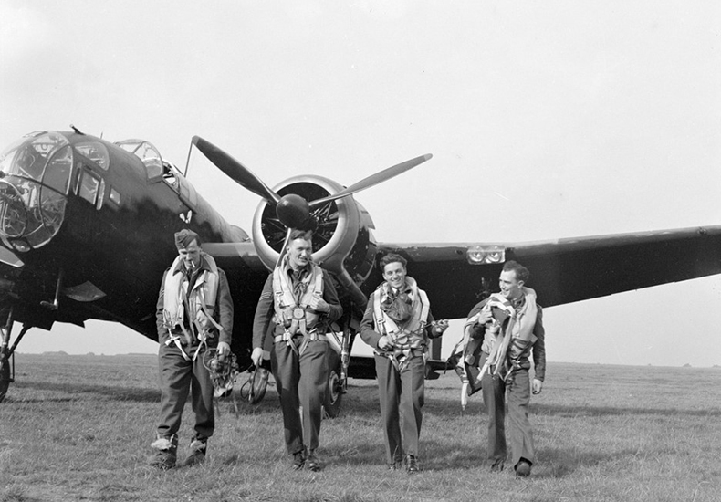 Black and white photo of four air force members walking away from a plane. Part of the Pathway to the Stars: A Centennial Celebration of Oakville’s Contributions to the Royal Canadian Air Force exhibit at Oakville Museum.