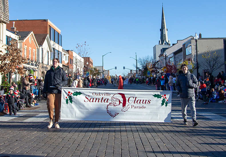 Volunteers walk down Lakeshore Road in Downtown Oakville carrying a Santa Claus Parade banner.