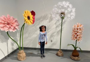 A child standing beside giant paper flowers at the Art in Full Bloom: Paper Botanicals workshop at Oakville Museum during Culture Days 2024. 